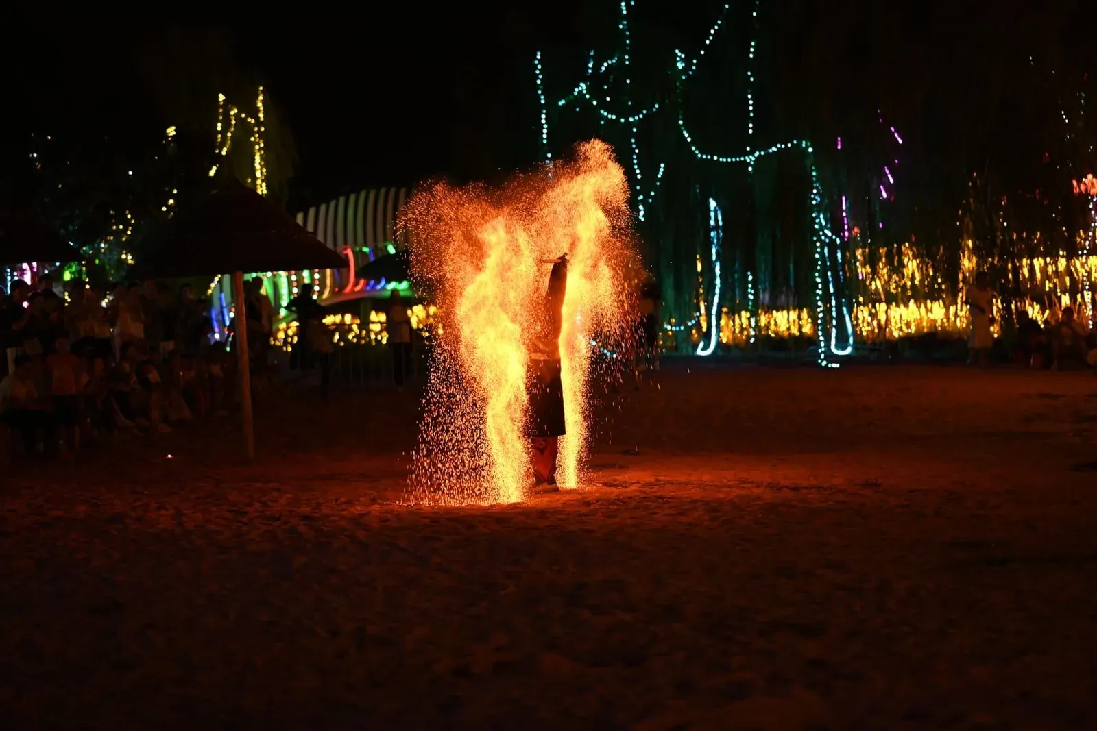 Fire performer on a Koh Samui beach at night with onlookers gathered around the flames