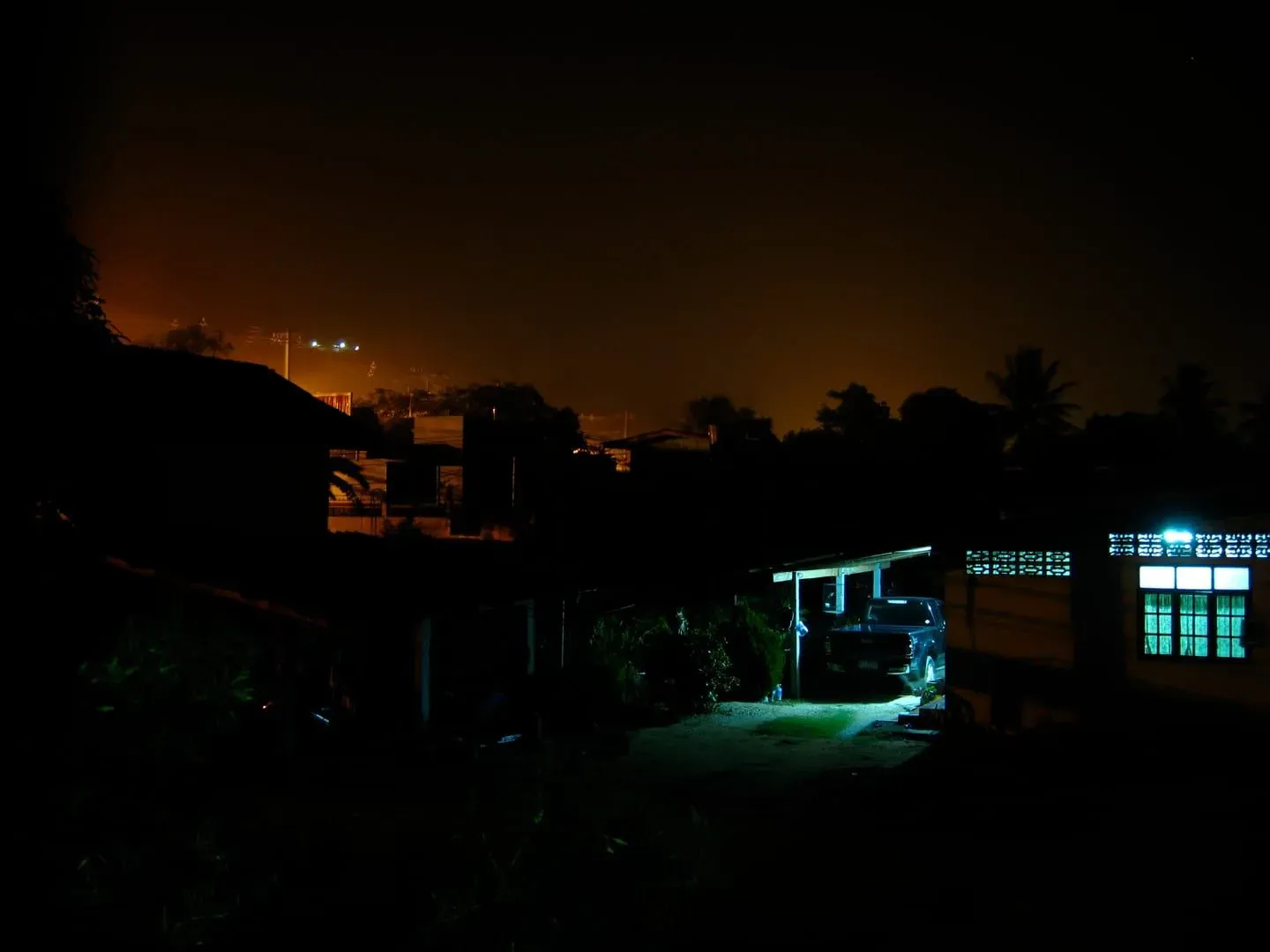 A hillside neighborhood near Ban Tai, Koh Samui, lit up after dark with a further hill silhouette behind it