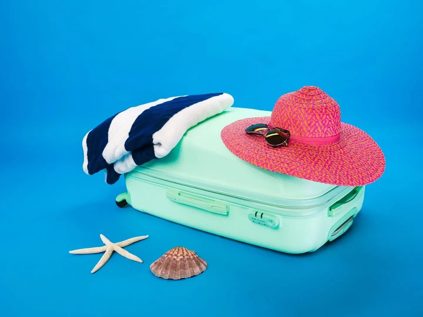 Open suitcase packed with a sun hat, beach towel and seashells for a Koh Samui packing list