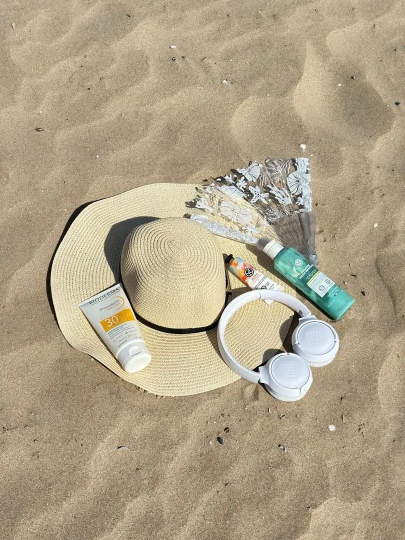 Flat lay of sun hat, sunscreen, portable fan and headphones for a Koh Samui rainy season packing list