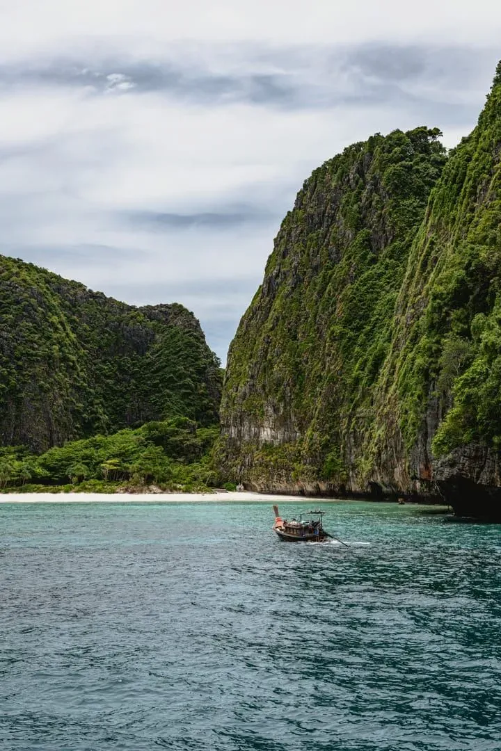 Longtail boat navigating rocky cliffs and clear water near Phuket Thailand coastline