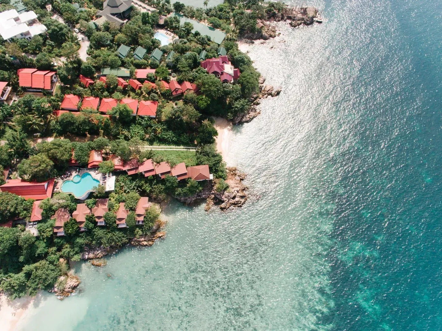 Aerial view of a tropical Koh Samui coastline with villas, lush greenery and clear turquoise water