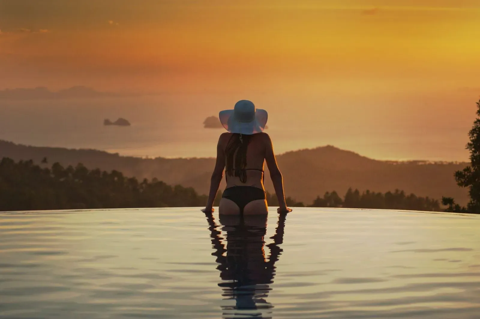 Woman relaxing at the edge of an infinity pool overlooking the sea at sunset near Koh Samui