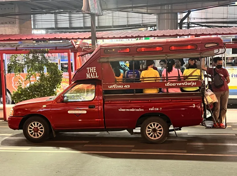 Camionnette songthaew rouge avec des passagers sur ses banquettes à un arrêt dans un village thaïlandais