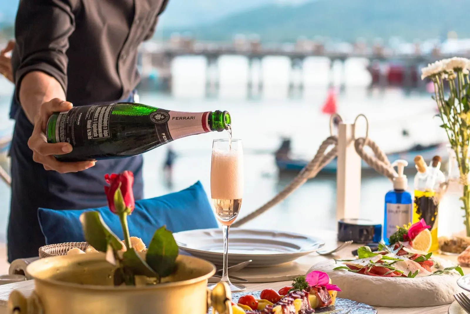 Waiter pouring wine at an elegant seaside dining table on Koh Samui at golden hour