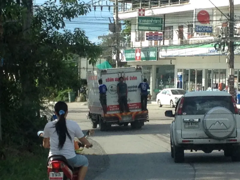 Circulation mixte d'un scooter, d'un camion de livraison et d'un SUV dans une rue de village de Koh Samui