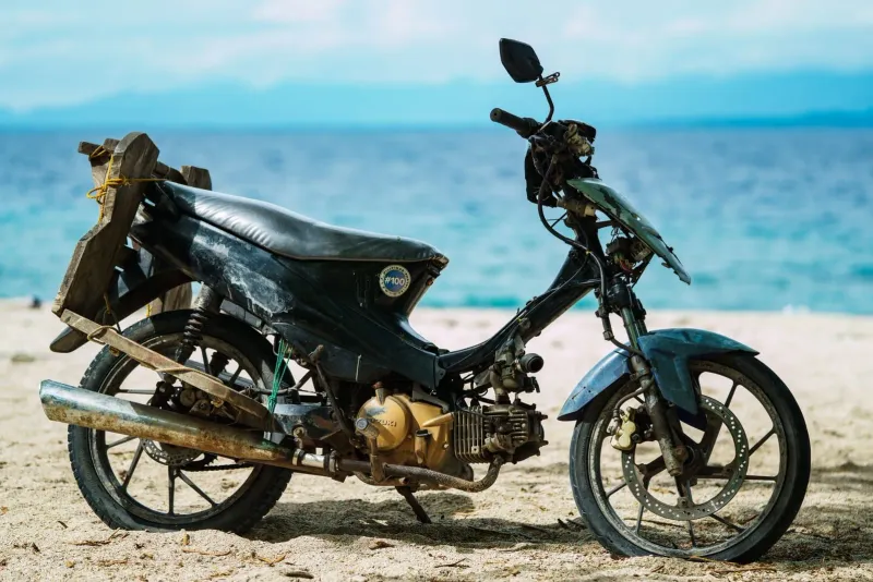 Weathered motorcycle parked on a sandy beach, a reminder to check scooter safety in Koh Samui
