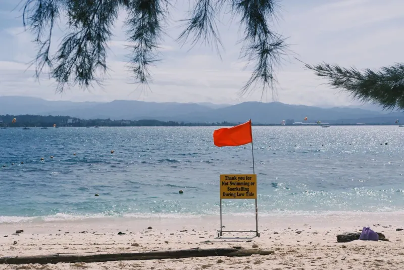 Tranquil beach scene with a red warning flag and low tide sign near Koh Samui