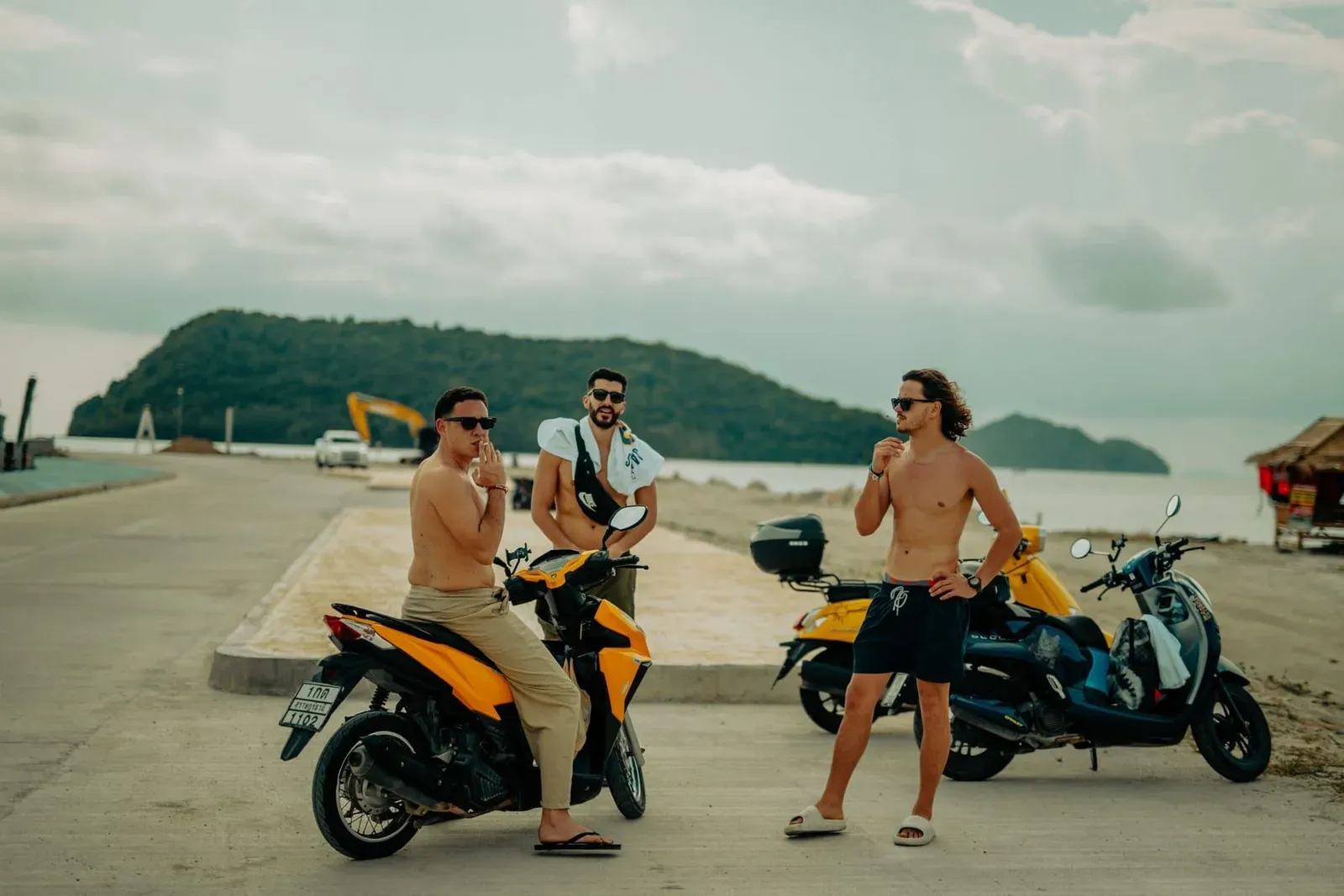 Tourists with rented scooters standing near a pier with island views in the background