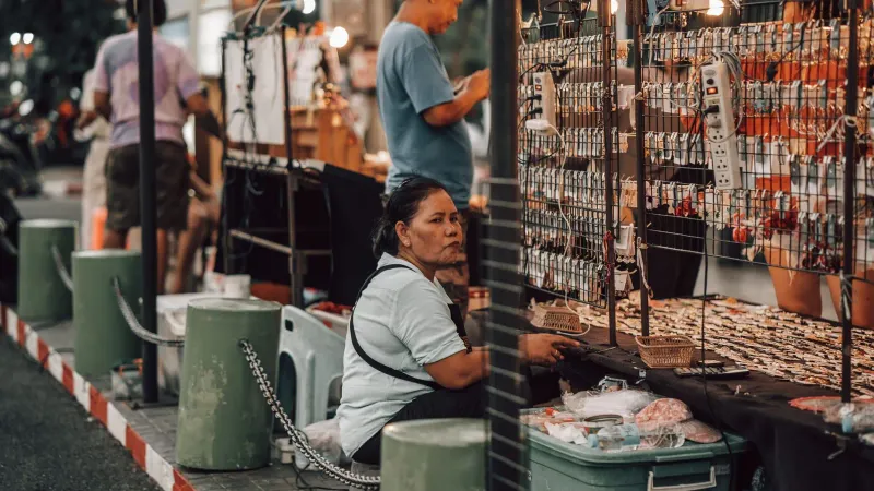 Vendor seated behind a market stall selling assorted merchandise in Thailand