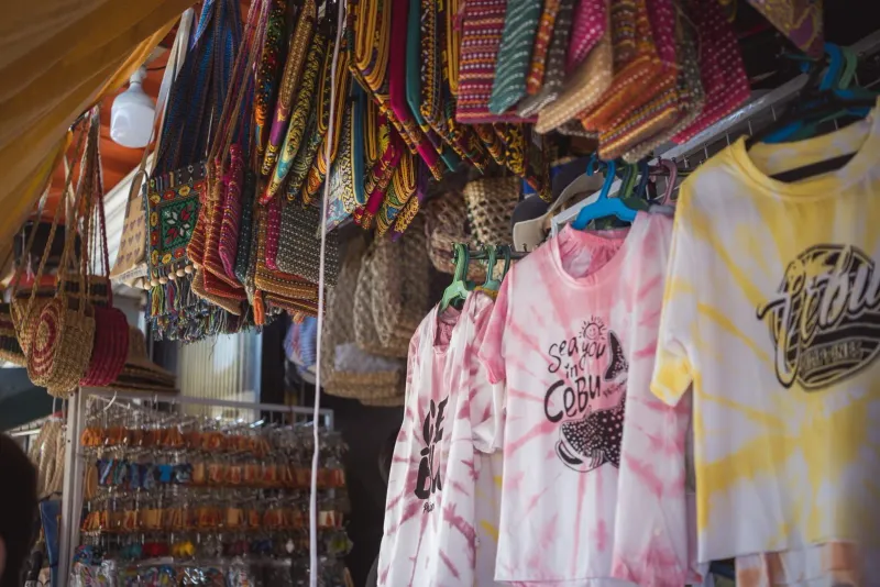 Colorful bags and printed t-shirts hanging for sale at a Koh Samui souvenir stall