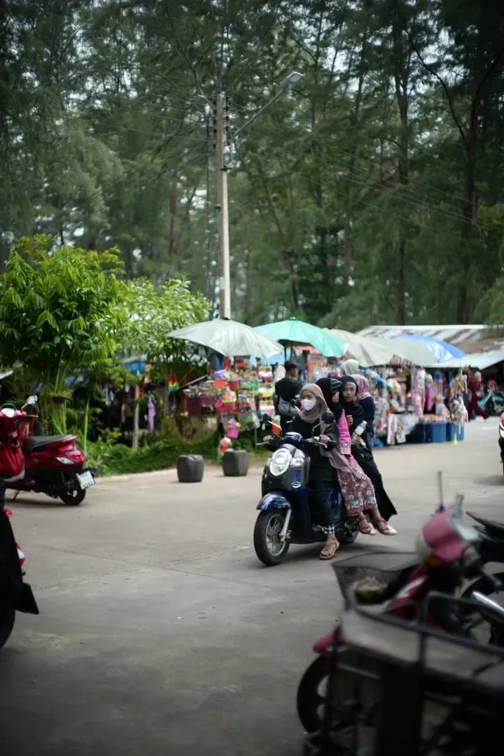 Scooter riders passing a vibrant Thai street market similar to Koh Samui's local markets