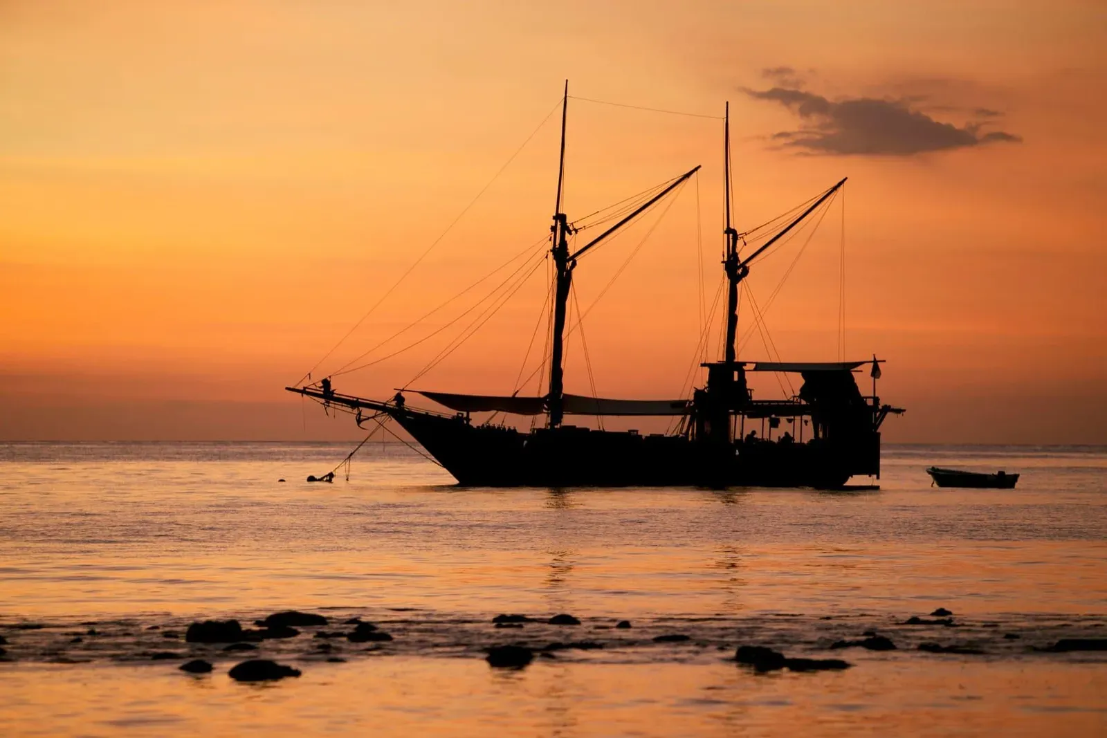 Classic sailboat silhouette against an orange sunset sky representing a Koh Samui sunset cruise charter