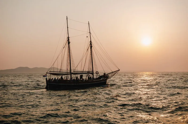 Voilier traditionnel glissant sur l'océan au coucher du soleil, avec des montagnes en arrière-plan à Koh Samui