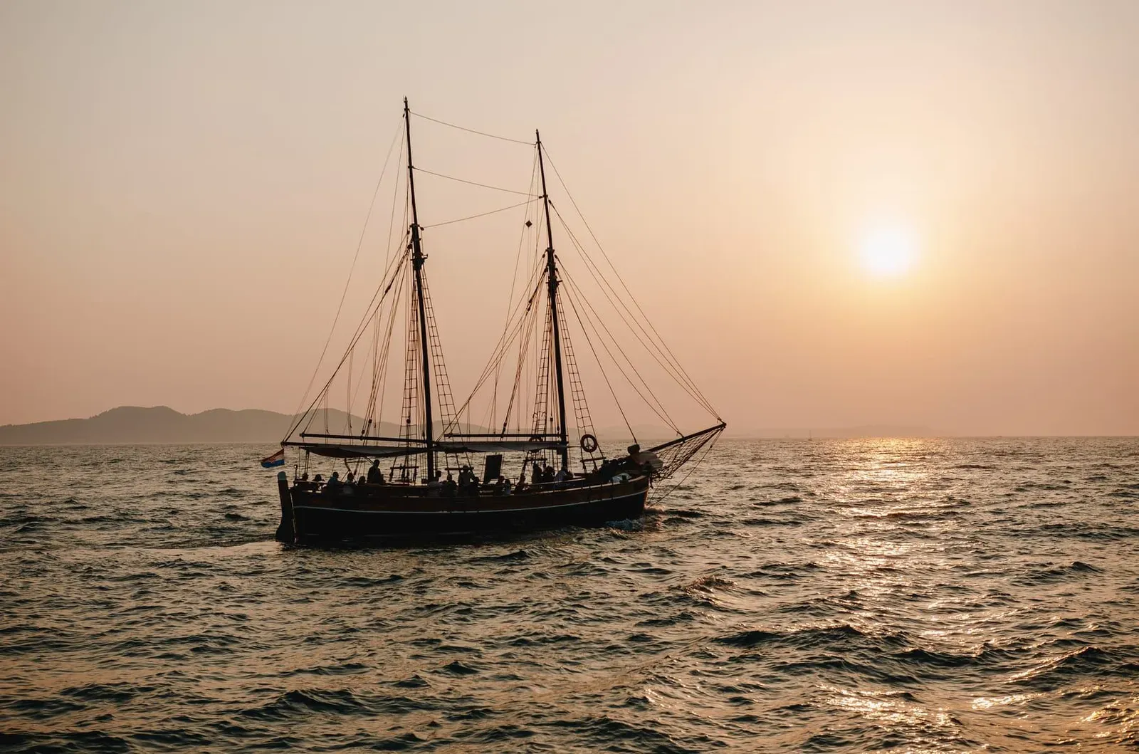 Traditional sailboat gliding across the ocean at sunset with mountains behind Koh Samui