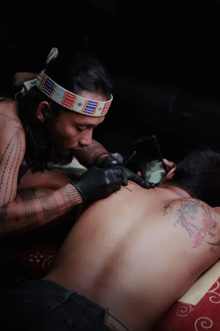 Traditional hand-tattooing artist in Southeast Asia inks intricate patterns onto a client's back using a hand-poke technique