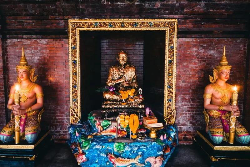 Golden Buddha statue flanked by guardian figures inside a Thai temple hall