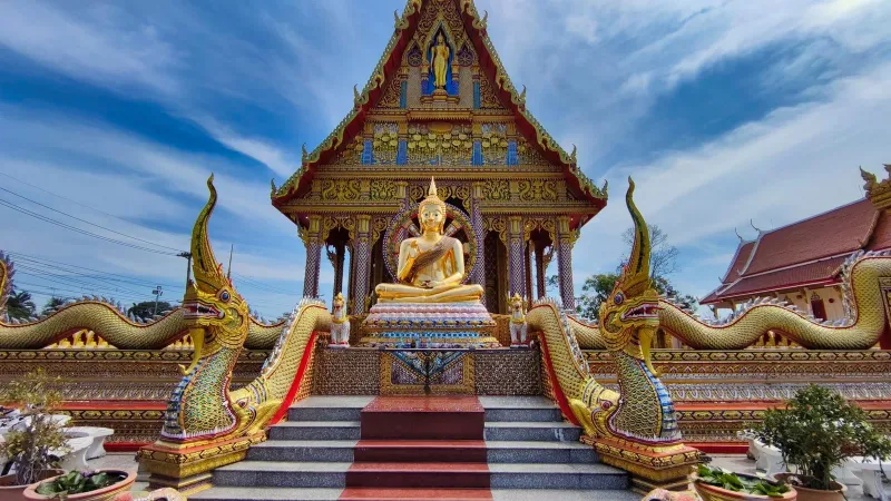 Rows of golden Buddha statues inside a richly decorated Thai temple viharn