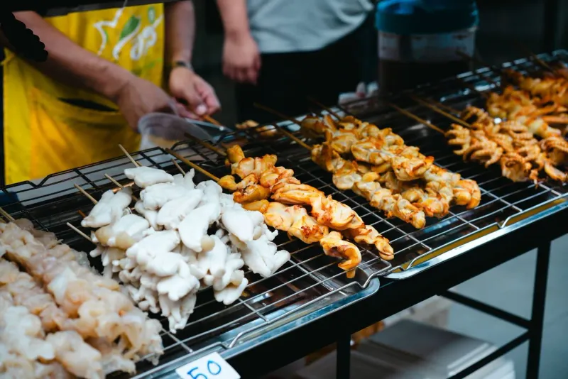 Skewers grilling over charcoal at a lively Koh Samui food market stand