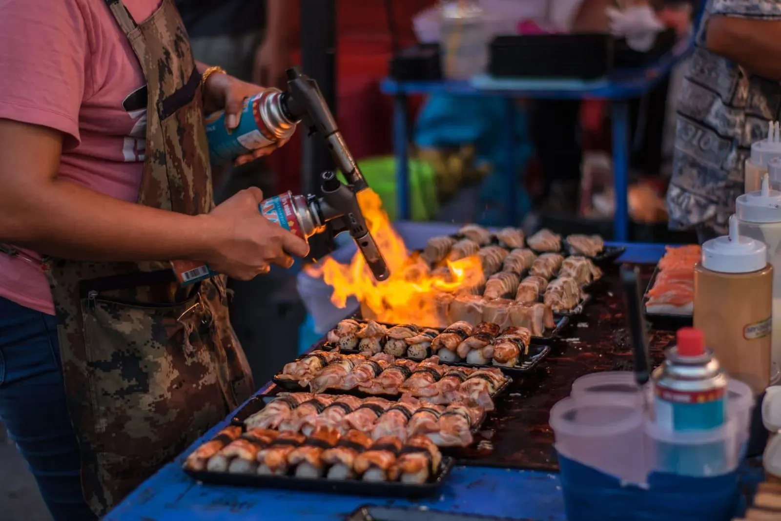 Street food vendor grilling skewers over open flame at a Thai night market stall