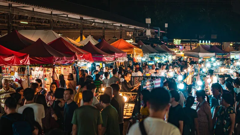 Crowds of shoppers browsing tented stalls at a busy Thai night market