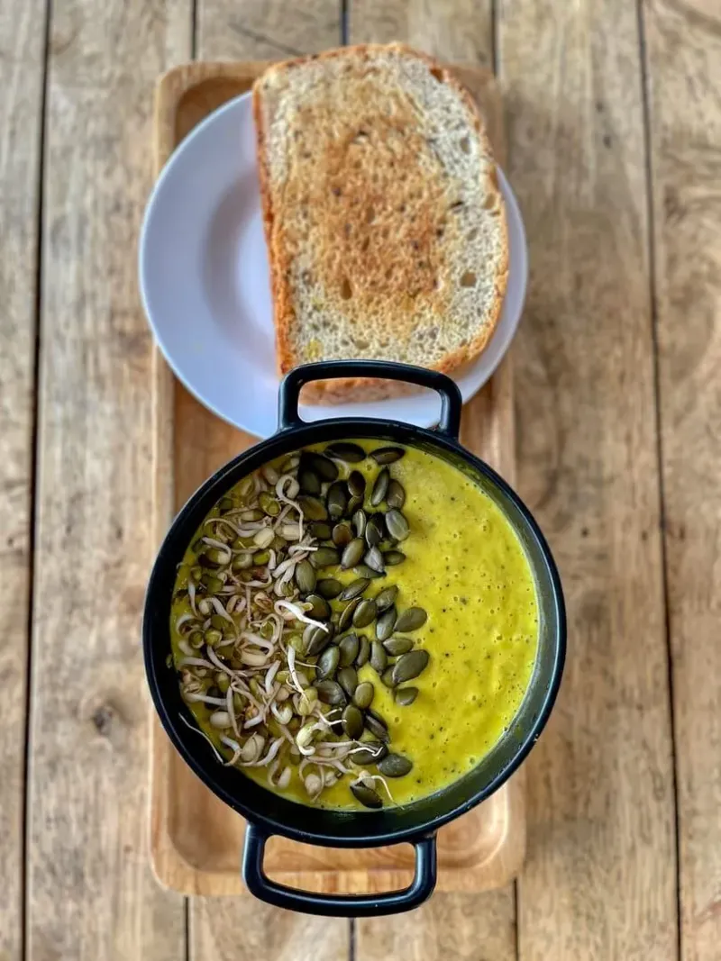Vegan pumpkin soup garnished with seeds and sprouts on a wooden table