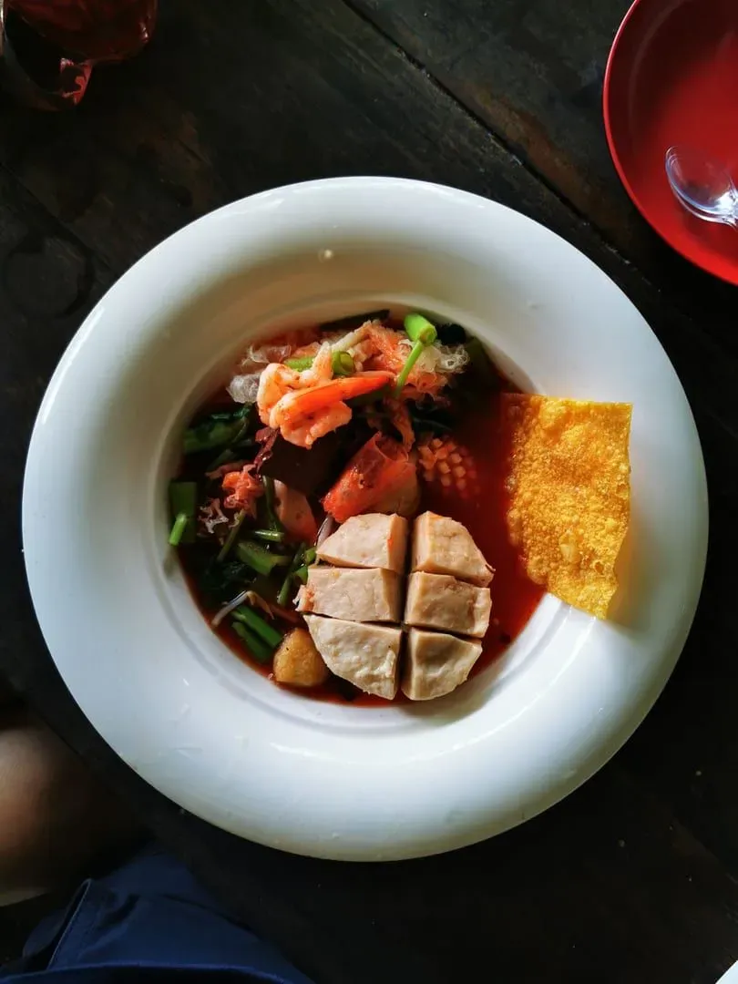 Thai tom yum soup garnished with fresh vegetables on a wooden table in Koh Samui