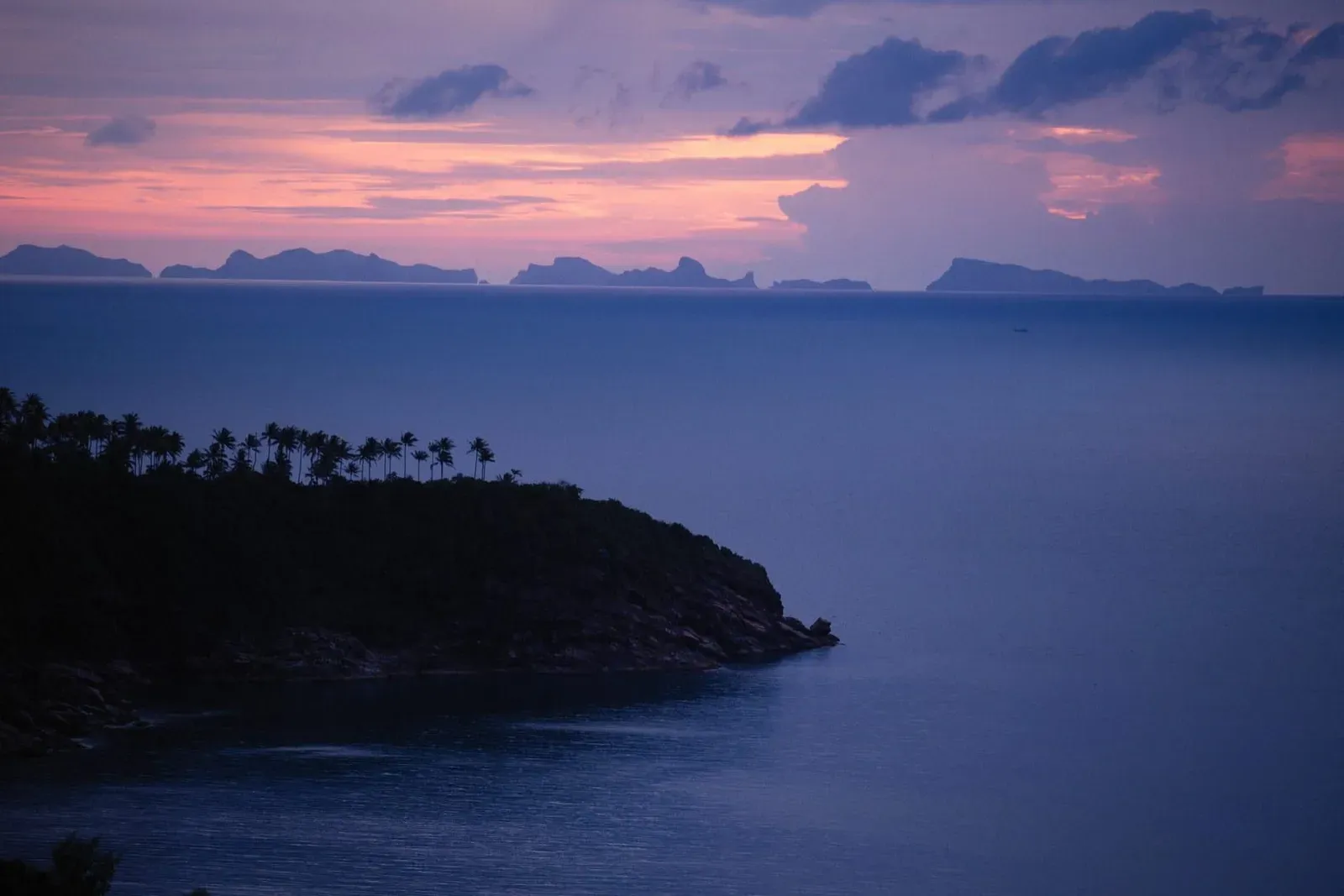 Silhouetted palm trees and distant limestone islands at sunset near Ang Thong Marine Park Koh Samui