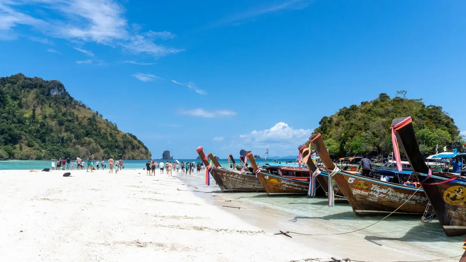 Longtail boats on a tropical beach beneath limestone cliffs on Thailand's Andaman coast