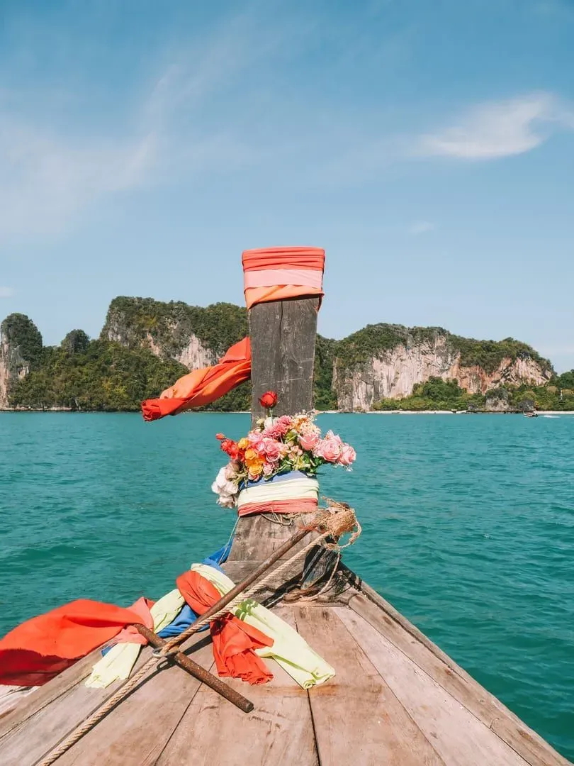 Decorated longtail boat on turquoise water near limestone cliffs typical of the Krabi coast