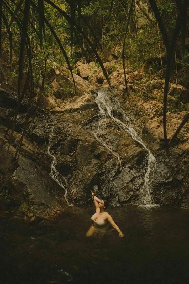 Woman swimming in a natural pool below a jungle waterfall on a Koh Samui hiking trail