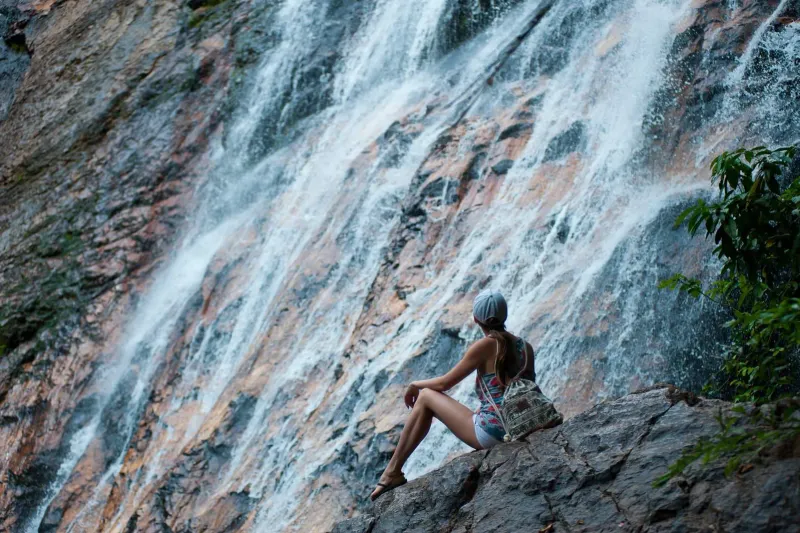 Escursionista seduto sulle rocce accanto a una cascata, durante un trekking panoramico a Koh Samui