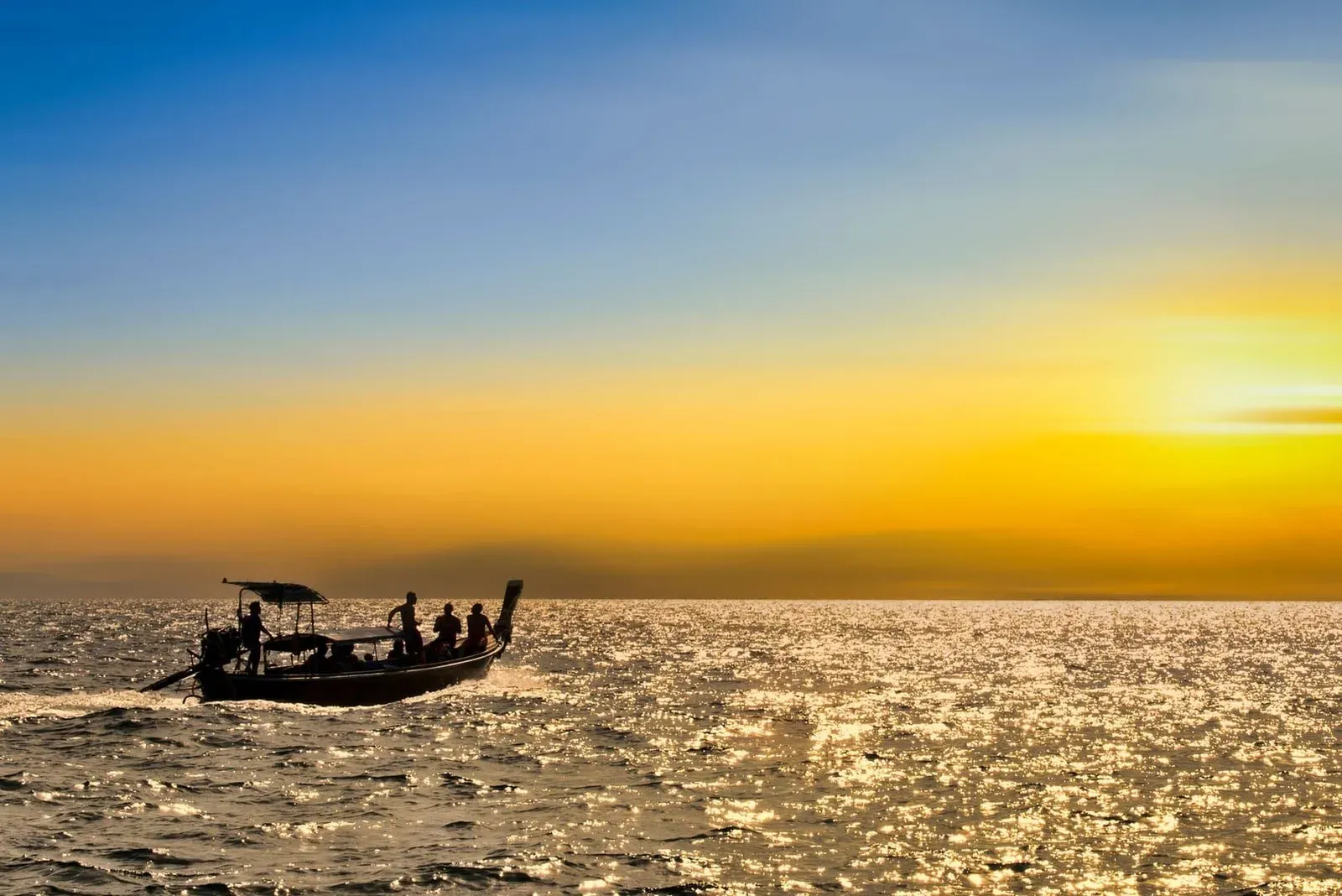 Silhouette of a traditional wooden boat crossing calm water at sunset near Koh Samui