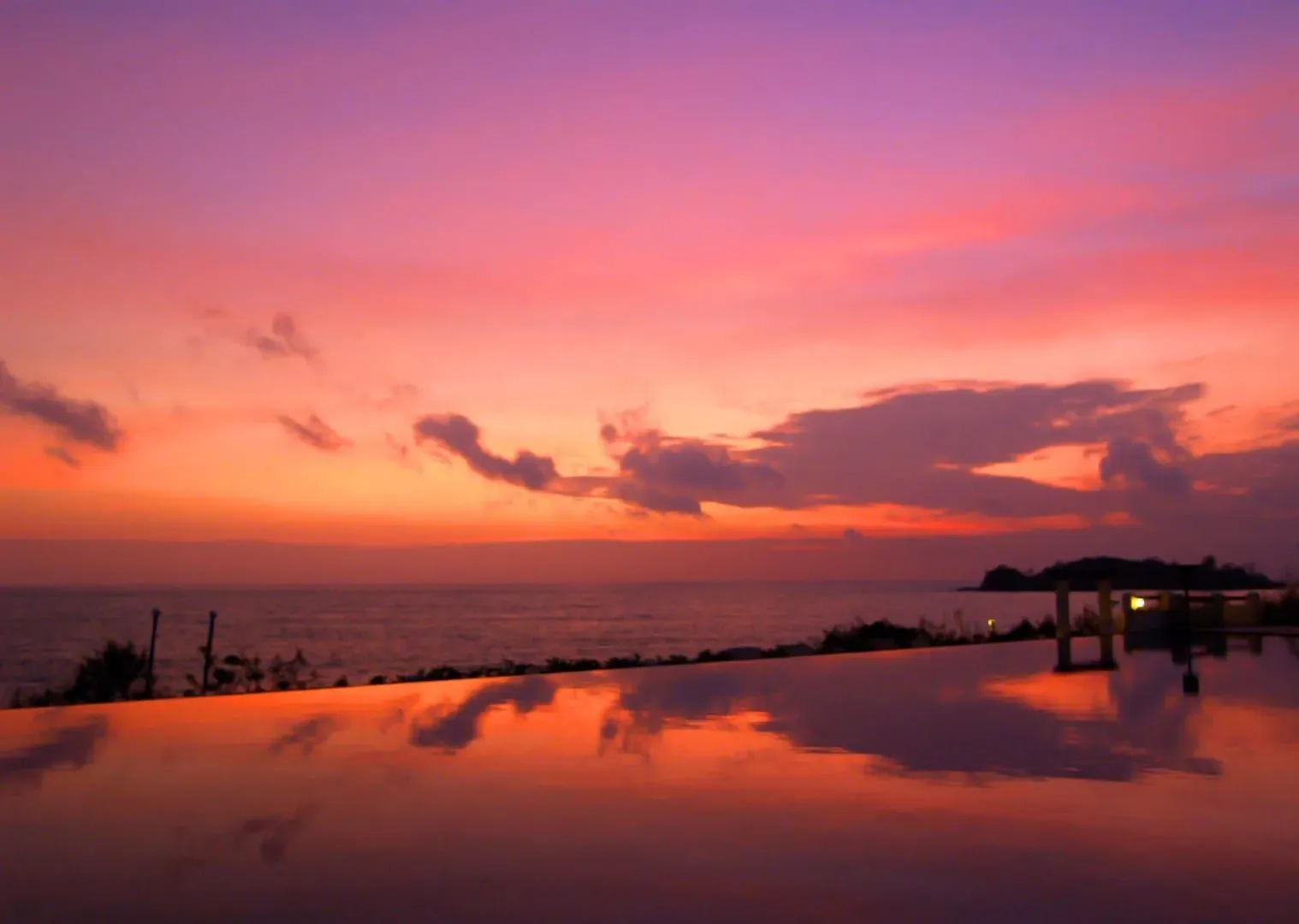 Sunset over the sea with a headland silhouette, seen from a beachfront terrace on Koh Samui's northwest coast