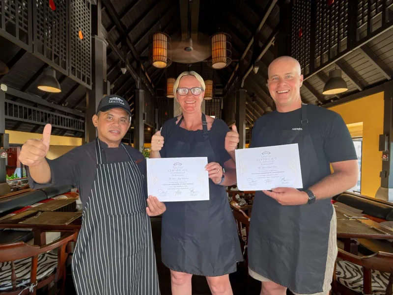 Guests holding certificates after a Thai cooking class in an open-air hall