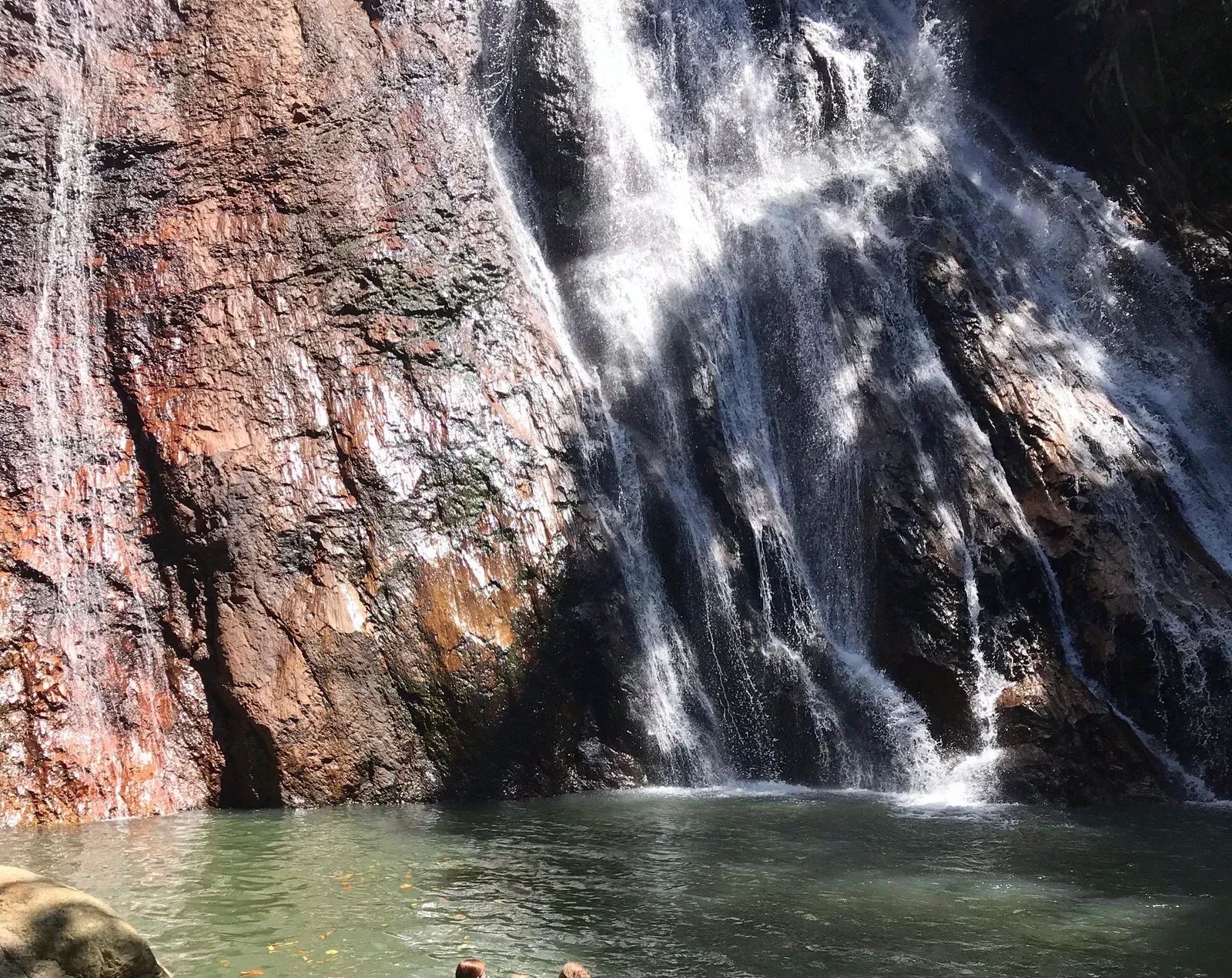 Sonnenbeschienene Granitwand bei Lat Wanon, an der Wasser in ein Schwimmbecken darunter fließt
