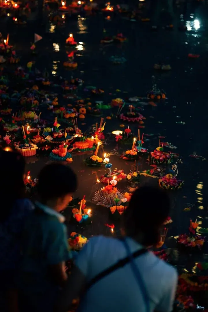 Participants releasing decorated floating krathong offerings onto the water at night during a Thai festival