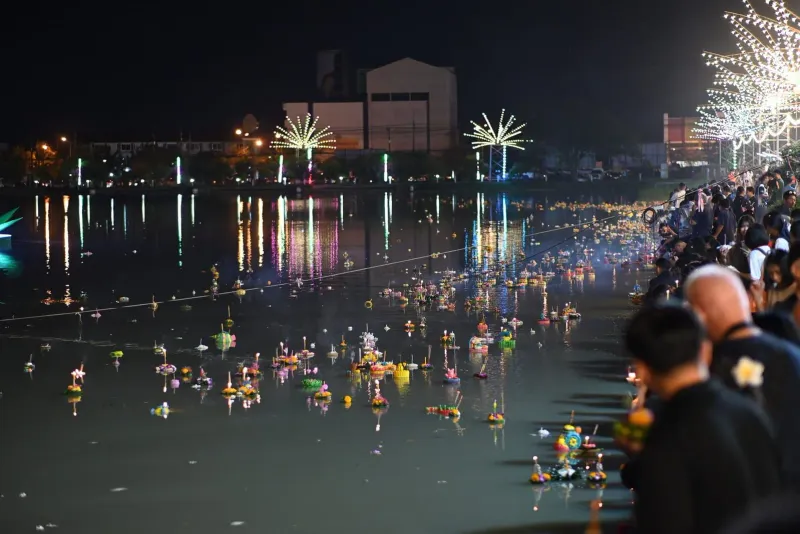 Crowds gathered along a shoreline at night floating illuminated krathong offerings during Loy Krathong