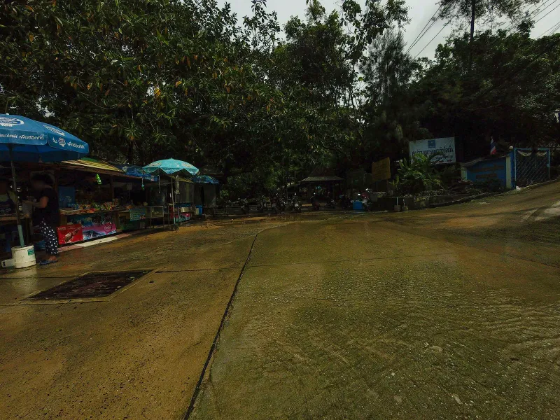 Motorbike parking area at the Hin Lad trailhead, shaded by tall trees