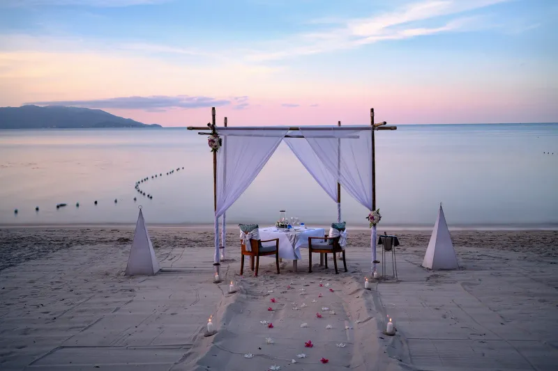 夕暮れに、白い天蓋とランタンで飾られたMelati Beach Resortのビーチディナーの席