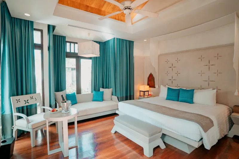 Melati Beach Resortのスイートにある、ターコイズのカーテン、チーク材の床、白いベッドの寝室