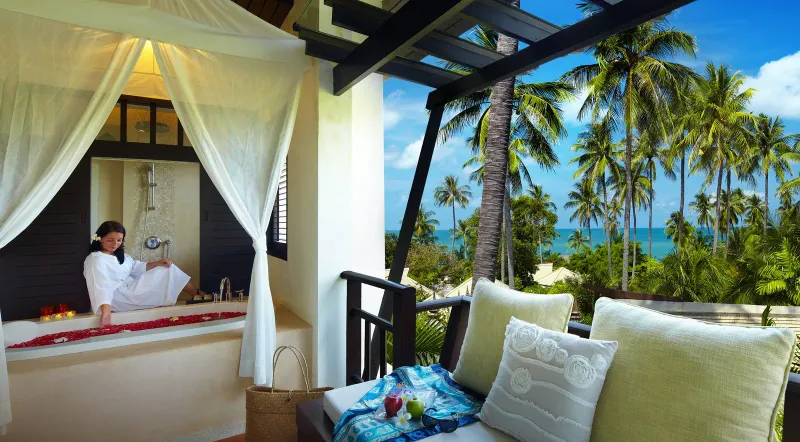 Melati Beach Resortの、白いカーテンとヤシ越しの海を望むバルコニーのバスタブ