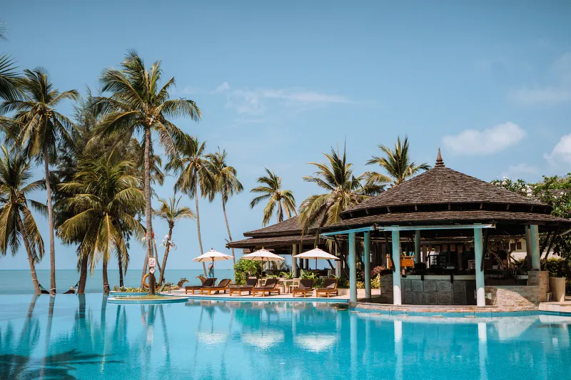 湾を見下ろすMelati Beach Resortのインフィニティプールと、ヤシに囲まれた茅葺きのプールバー