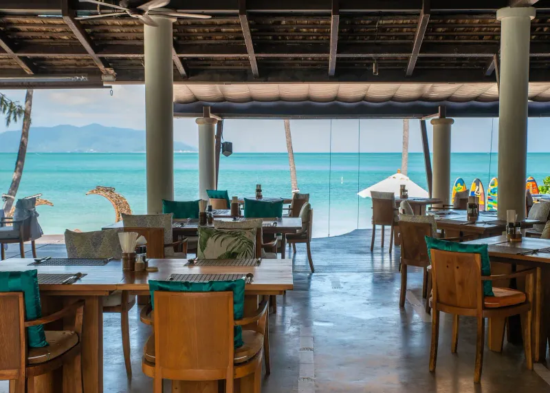 Melati Beach Resortの、湾に面したターコイズ色の椅子が並ぶビーチフロントのレストランテラス