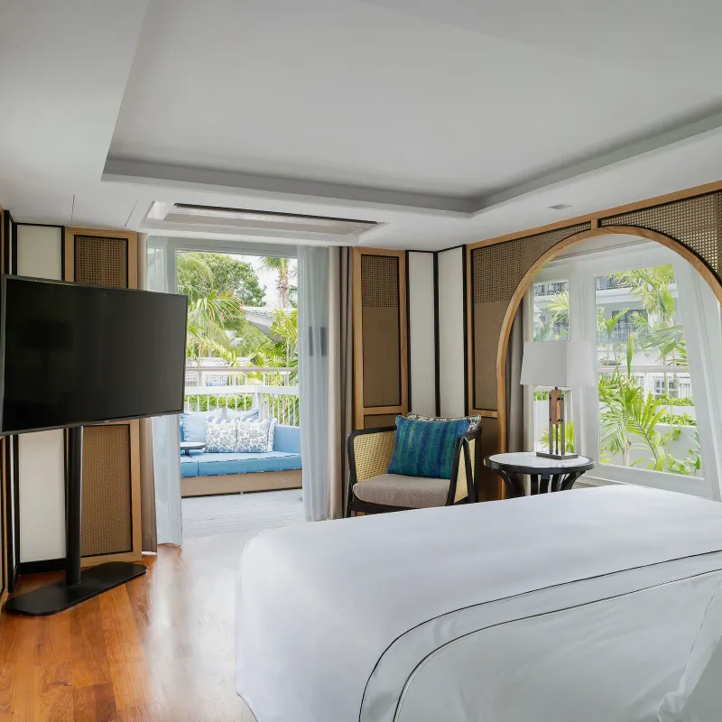 Camera da letto di una boat suite del Melia Koh Samui con pannelli ad arco di rattan, pavimento di teak e un divano in terrazza
