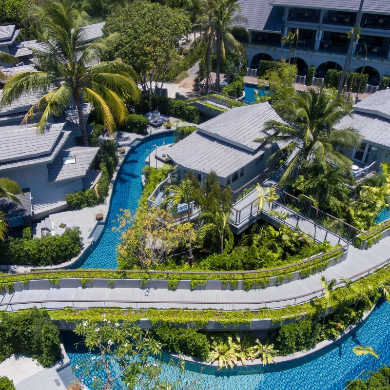 Veduta aerea del fiume lento del Melia Koh Samui che serpeggia tra suite a bordo piscina, palme e passerelle di legno