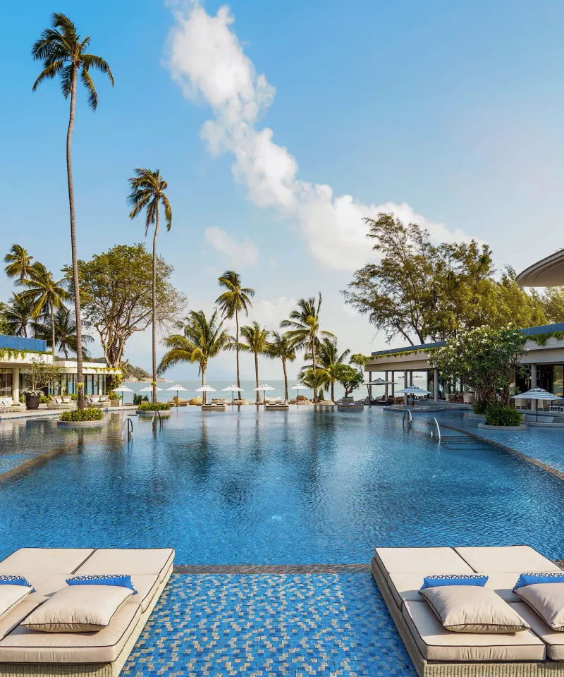 Piscina del Melia Koh Samui con lettini, alte palme e ristoranti fronte spiaggia rivolti verso la baia