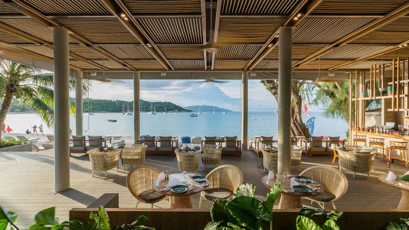 Ristorante all'aperto fronte spiaggia del Melia Koh Samui con sedie di rattan e barche a vela nella baia