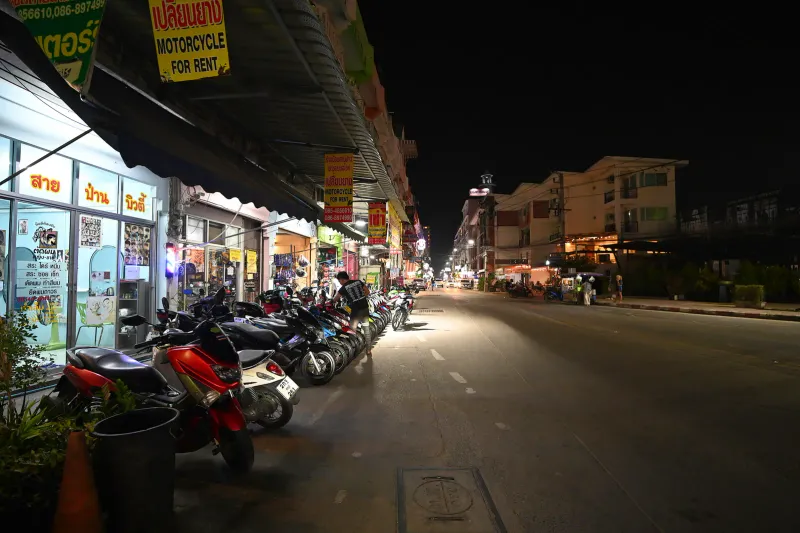 Fila di scooter parcheggiati accanto a negozi di noleggio in una strada thailandese di notte