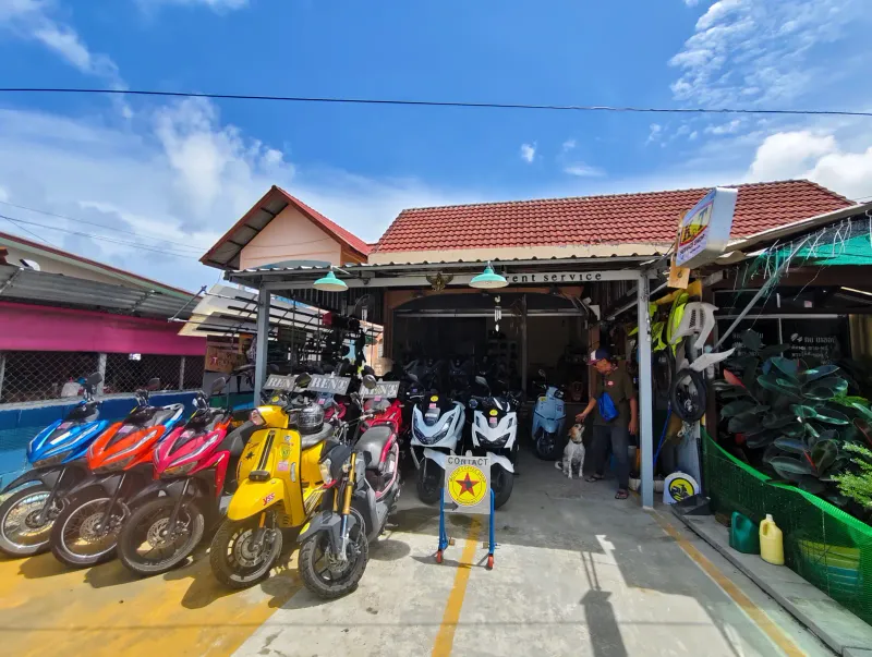 Piazzale di un noleggio scooter thailandese con file di scooter automatici colorati sotto un tetto di tegole